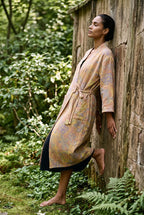 Bata kimono Kihada, jacquard botánico, melocotón: modelo apoyada en la pared, en un sendero de piedras en un jardín de musgo