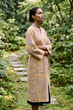Bata kimono Kihada, jacquard botánico, melocotón: modelo con las manos dentro de las mangas, en un sendero de piedras en un jardín de musgo