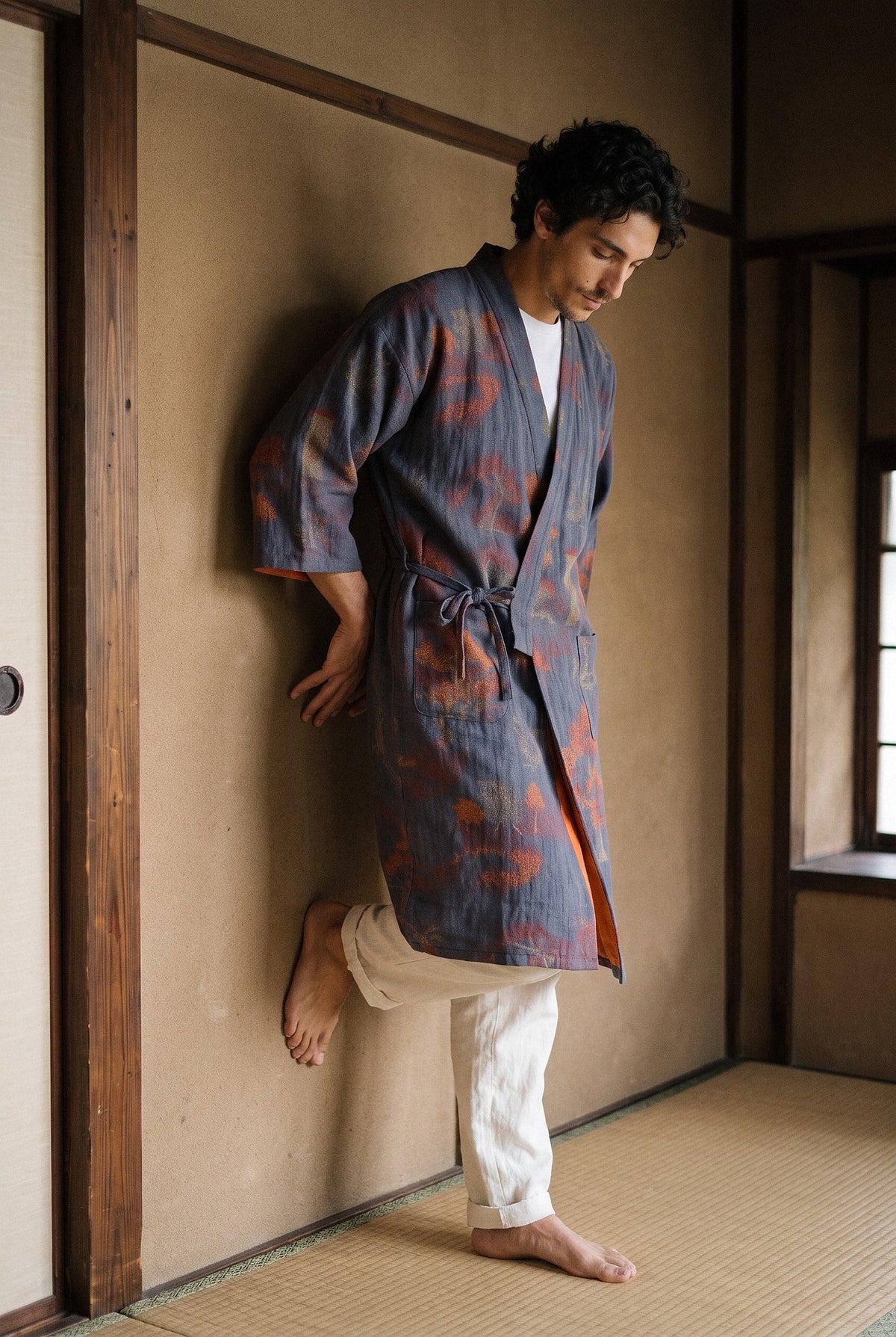 Bata kimono Momiji, jacquard azul marino: modelo apoyado en la pared, en una sala de té de madera oscura y muros de tierra