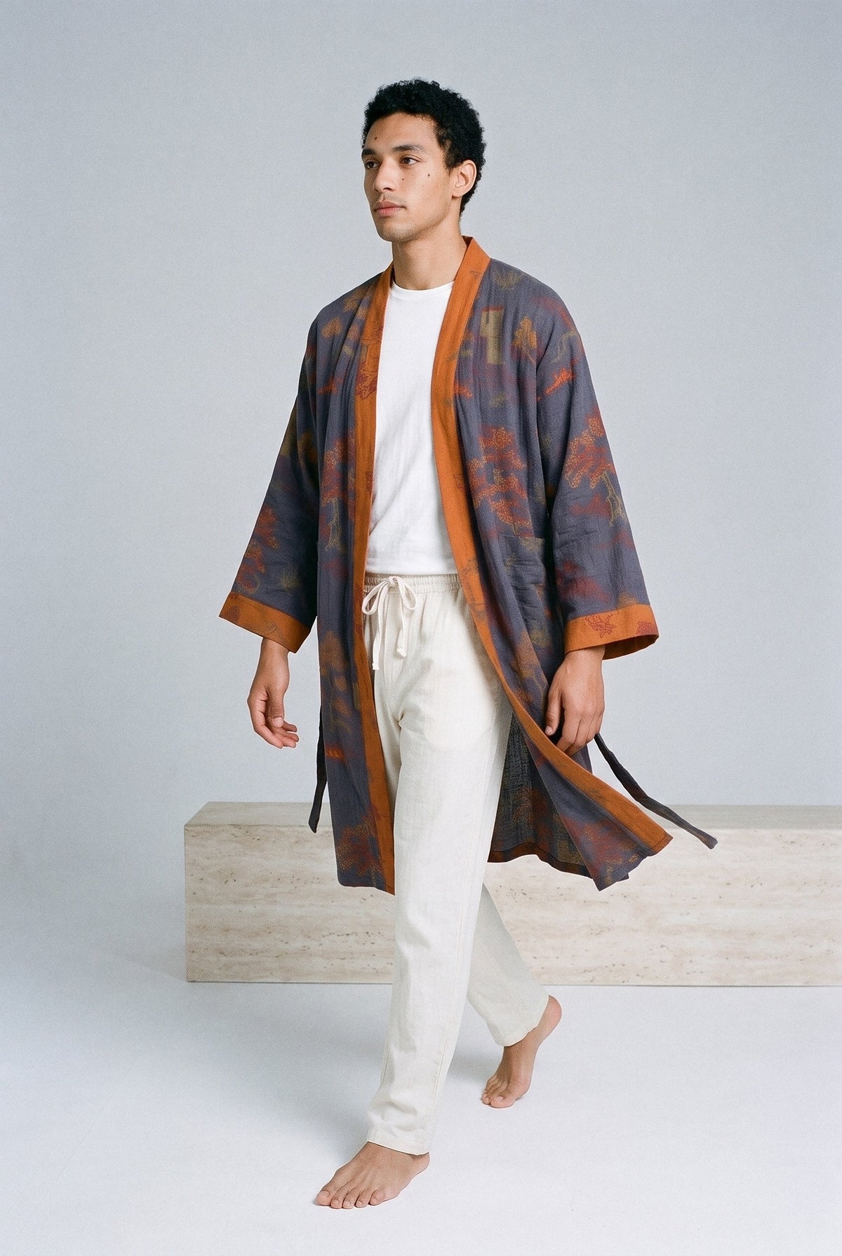 Bata kimono Ryokan, jacquard azul marino, hombre: modelo caminando, vista de tres cuartos, en estudio, fondo gris claro con peana de travertino