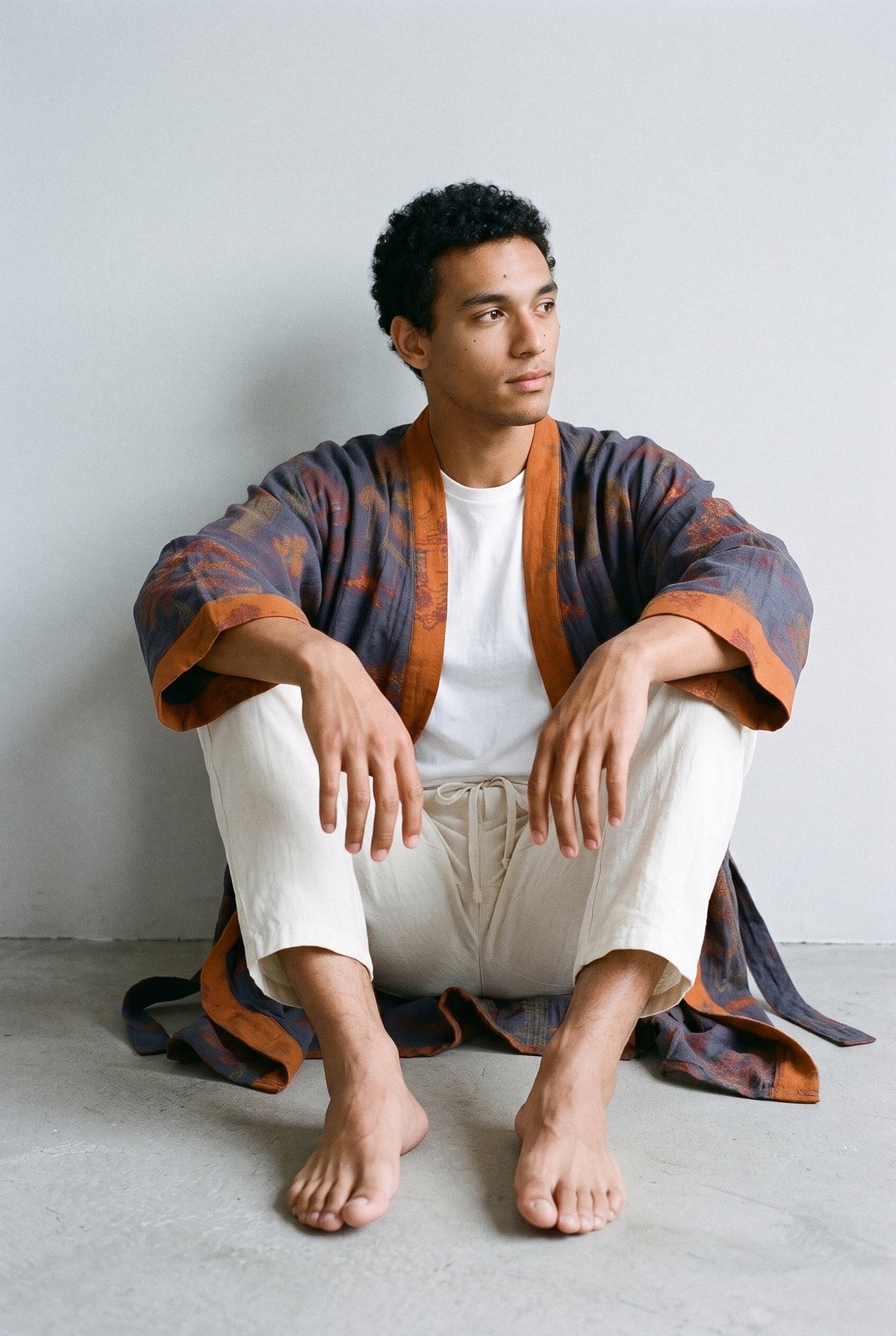 Bata kimono Ryokan, jacquard azul marino, hombre: modelo sentado contra la pared, en estudio, fondo gris claro con peana de travertino