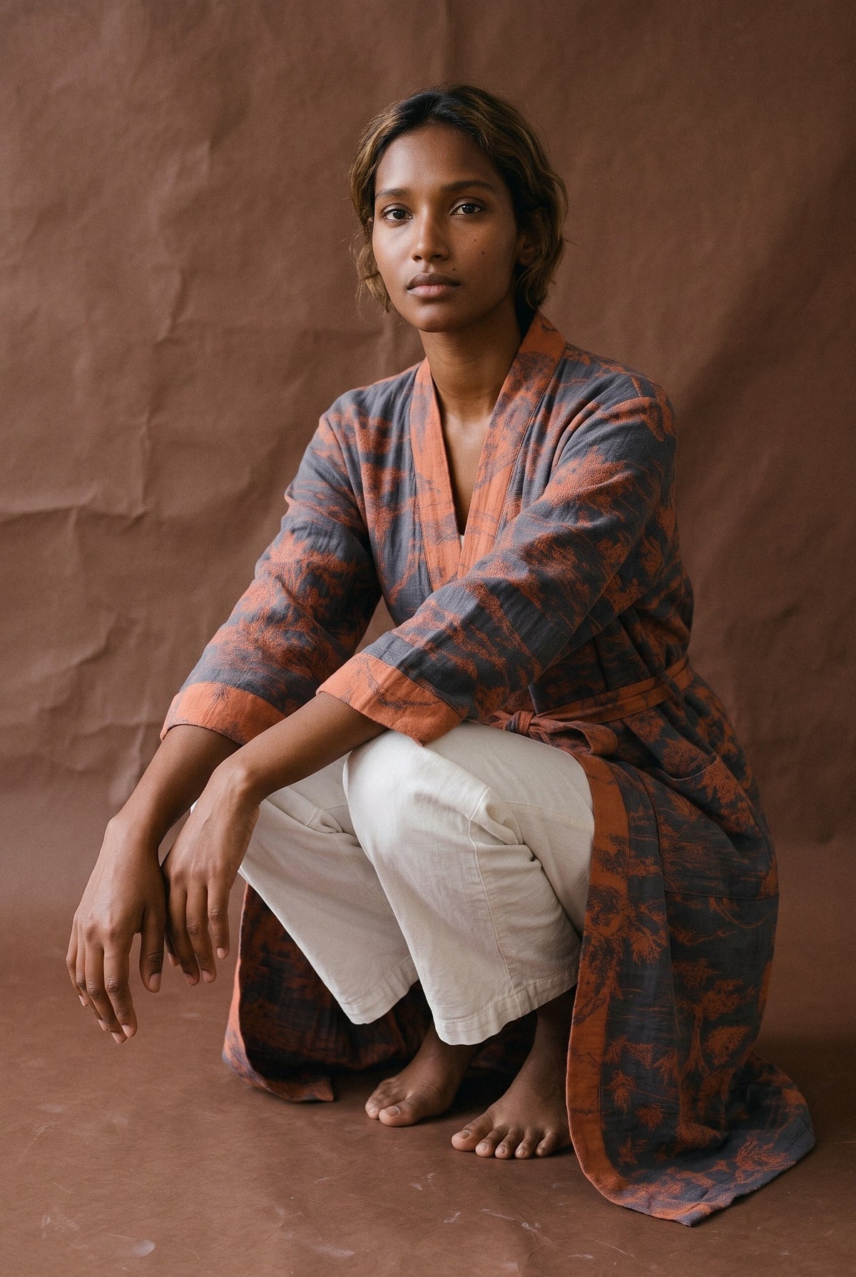 Bata kimono Ukiyo, algodón estampado, azul, mujer: modelo agachada, en estudio, fondo marrón chocolate