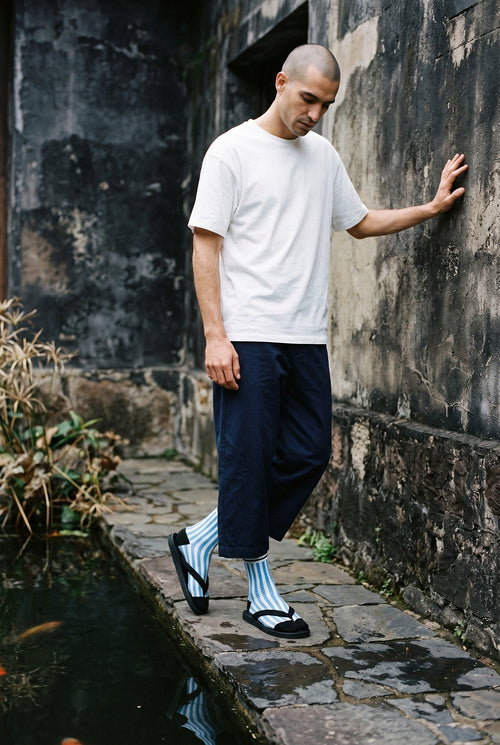 Calcetines tabi Miko, rayas, azul: modelo de puntillas, junto a un estanque de carpas con piedras oscuras