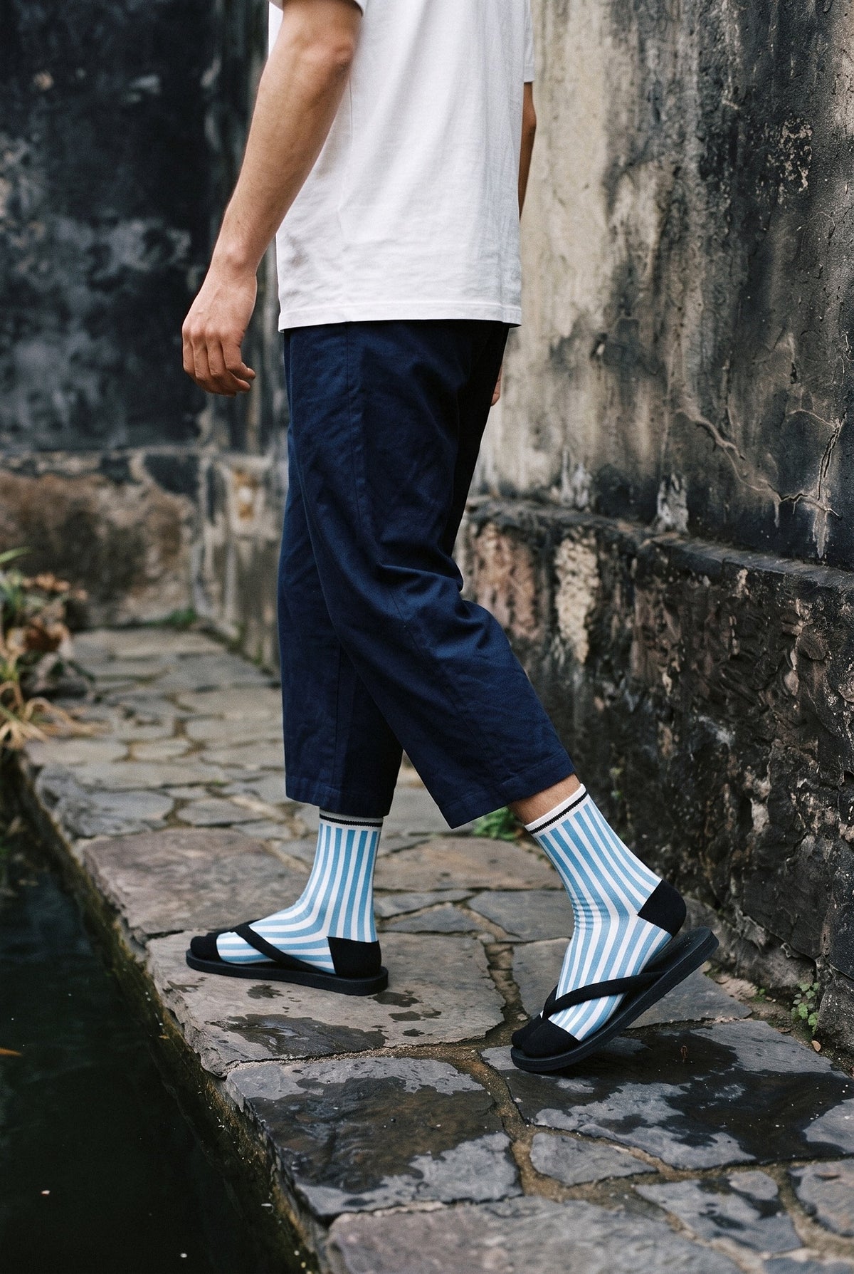 Calcetines tabi Miko, rayas, azul: modelo caminando, junto a un estanque de carpas con piedras oscuras