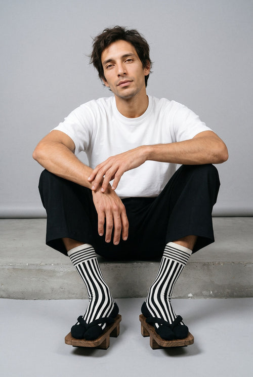 Calcetines tabi Miko, rayas, negro: modelo sentado en un escalón, en estudio, fondo gris perla