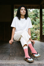 Calcetines tabi Miko, rayas, rojo: modelo sentada con los tobillos cruzados, en un pabellón de madera oscura abierto al jardín