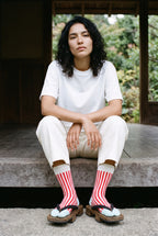 Calcetines tabi Miko, rayas, rojo: modelo sentada en un escalón, en un pabellón de madera oscura abierto al jardín