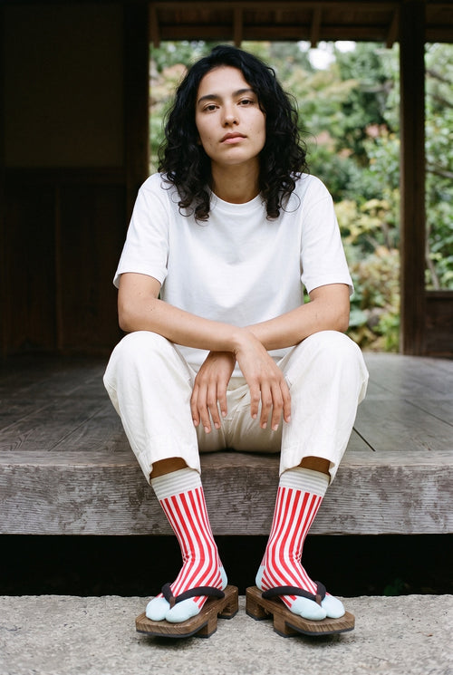 Calcetines tabi Miko, rayas, rojo: modelo sentada en un escalón, en un pabellón de madera oscura abierto al jardín