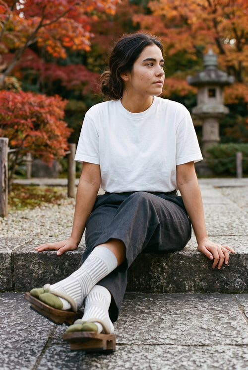 Calcetines tabi Sen, rayas, gris claro: modelo sentada con los tobillos cruzados, en un jardín japonés en otoño con arces rojos