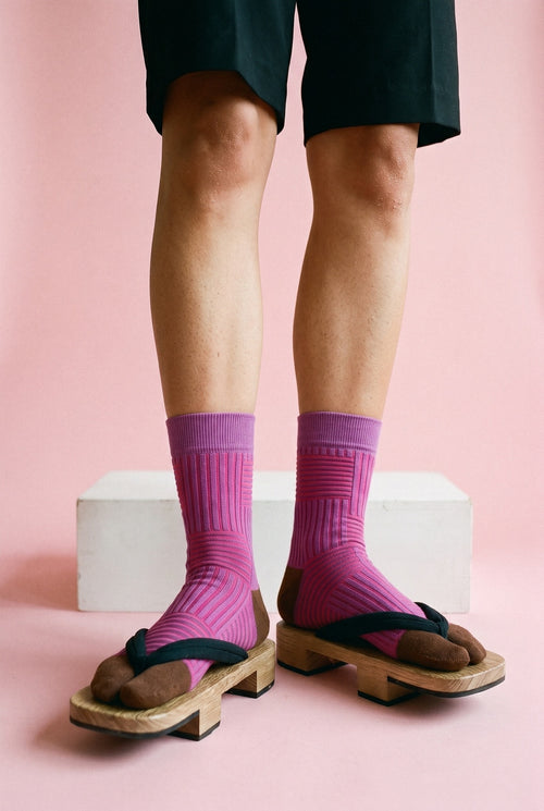 Calcetines tabi Sen, rayas, rosa fucsia: detalle de los calcetines, de la rodilla al pie, en estudio, fondo rosa empolvado con peana blanca