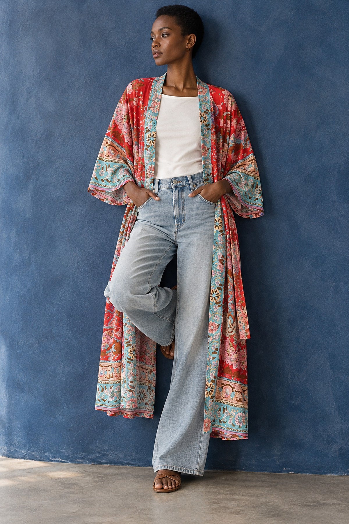 Kimono largo Hane multicolor abierto sobre top blanco y vaqueros anchos, apoyada en una pared índigo