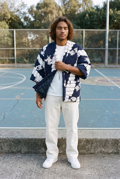 Chaqueta acolchada Aizome, hanten de estampado índigo: modelo con el tejido movido por la brisa, en una cancha de baloncesto de azul desvaído