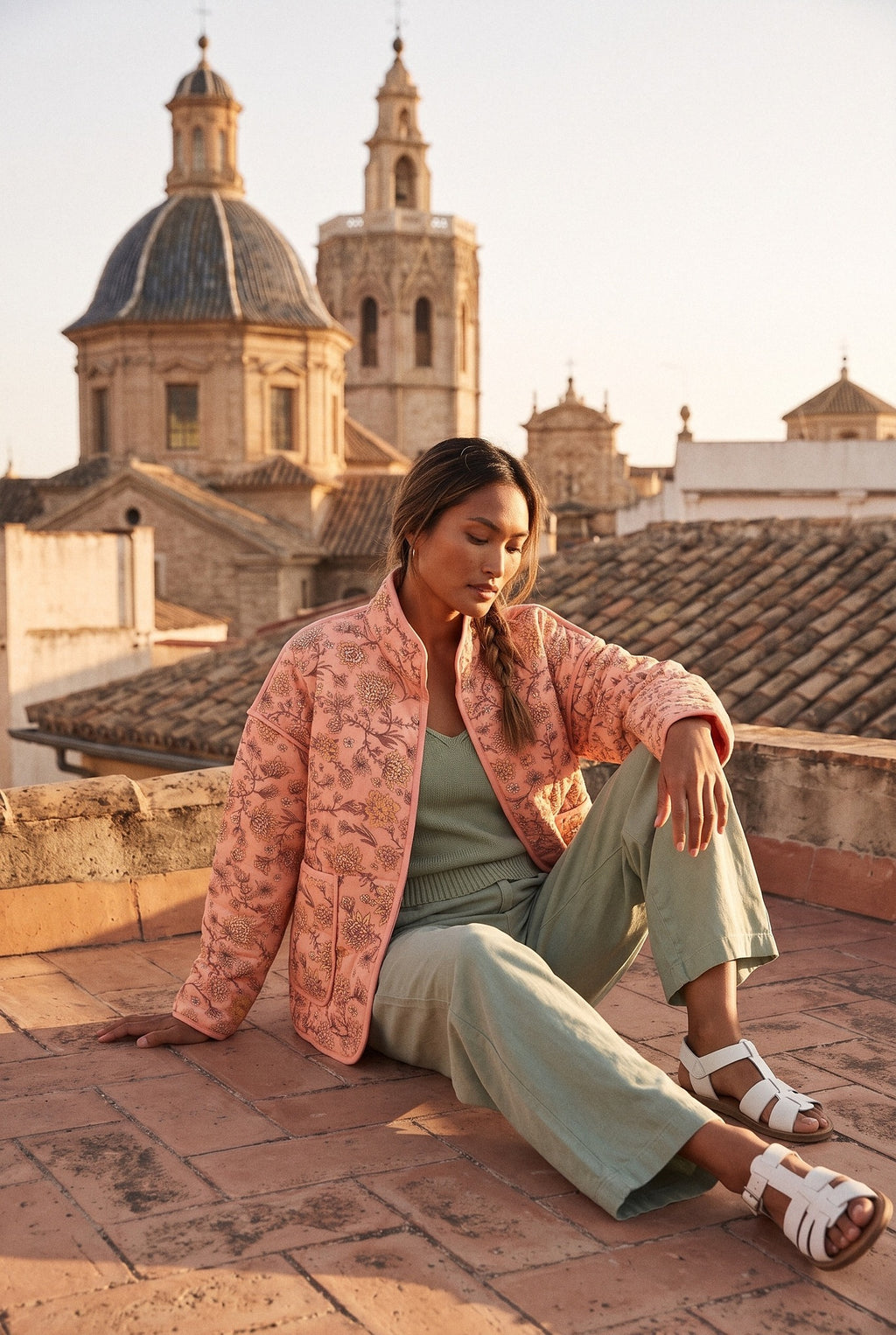 Chaqueta acolchada Benihana, flores, rosa salmón: modelo sentada en el suelo, en una azotea de Valencia con vistas a las cúpulas