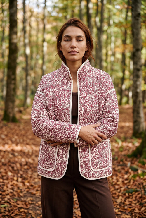 Chaqueta acolchada Hana, flores, rojo y crudo: modelo con los brazos cruzados, en un hayedo de Navarra en otoño