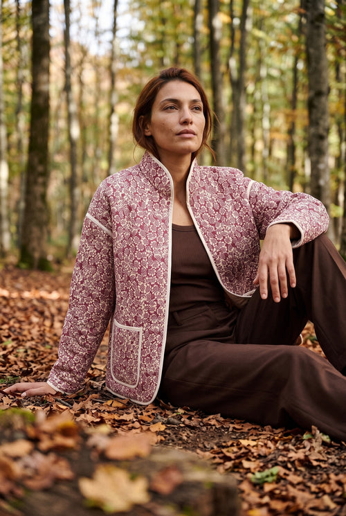 Chaqueta acolchada Hana, flores, rojo y crudo: modelo sentada en el suelo, en un hayedo de Navarra en otoño