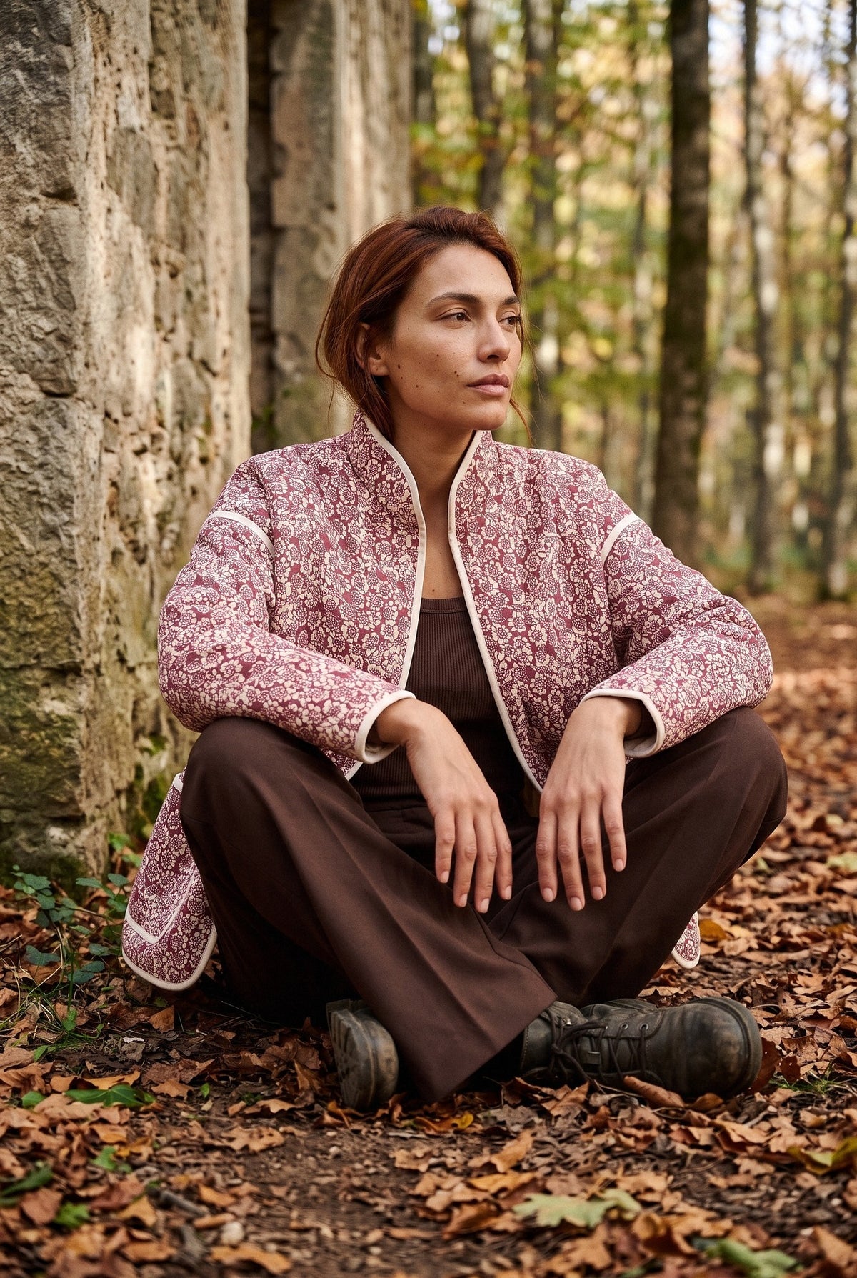 Chaqueta acolchada Hana, flores, rojo y crudo: modelo sentada contra la pared, en un hayedo de Navarra en otoño
