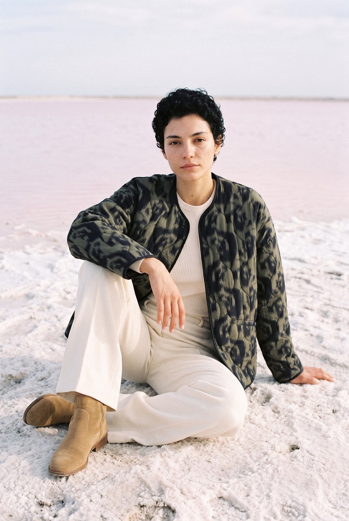 Chaqueta acolchada Shinrin, estampado ikat, verde bosque: modelo sentada en el suelo, junto a la laguna rosa de Torrevieja