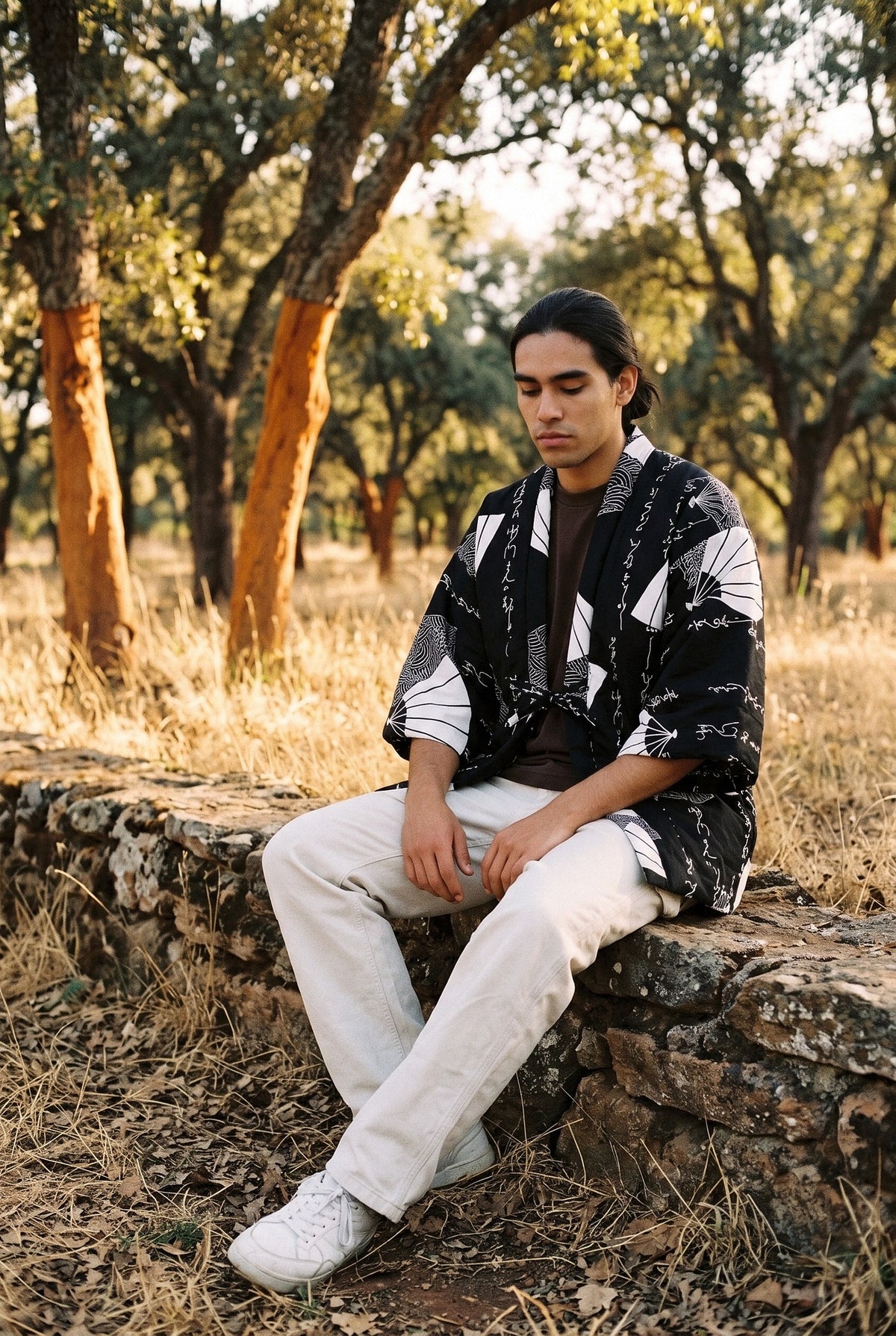 Chaqueta acolchada Shodō, hanten de caligrafía, negro y blanco: modelo sentado de lado con las piernas cruzadas, en un alcornocal de Extremadura