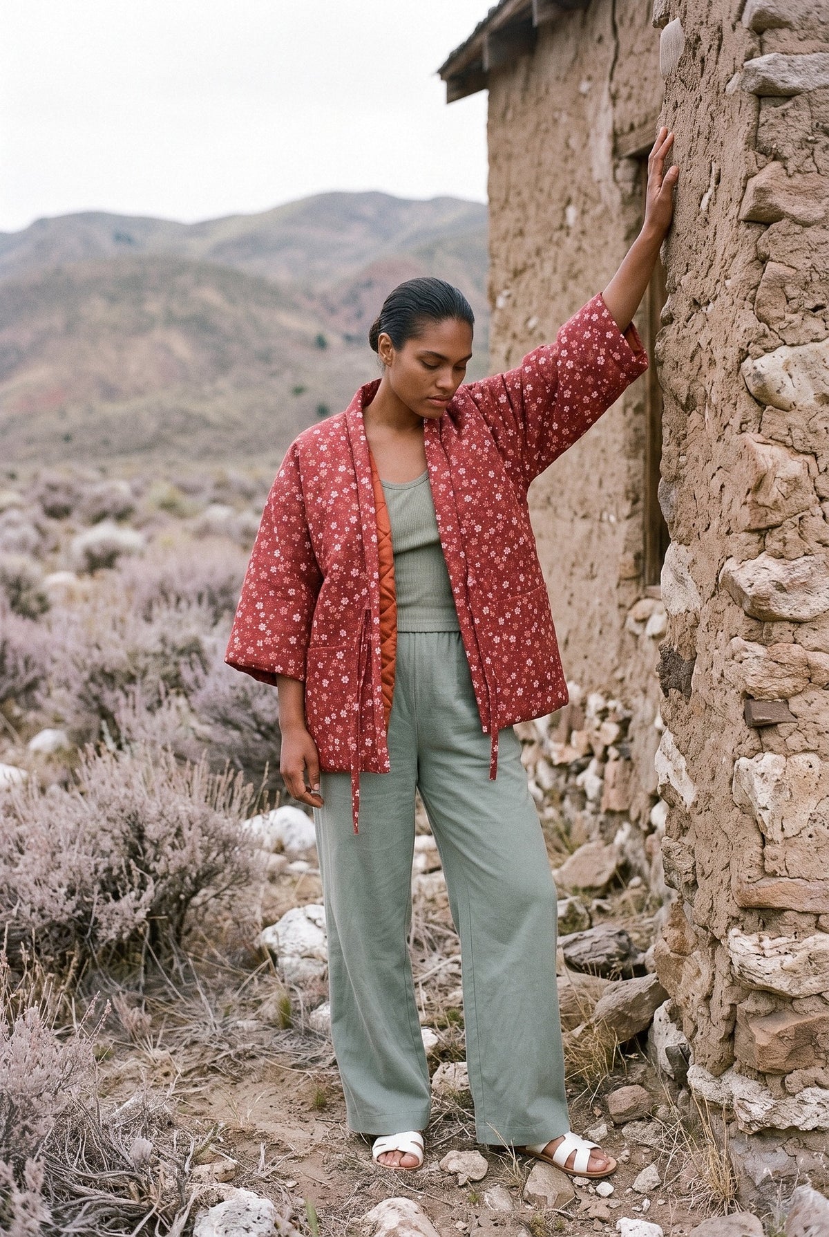 Chaqueta acolchada Tsubaki, hanten de florecillas, rojo: modelo con un brazo en alto, entre salvia seca y rocas blancas de Sierra Nevada