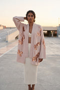 Chaqueta kimono Anzu, flores de lentejuelas, rosa empolvado: modelo con una mano en la nuca, en la azotea de un aparcamiento de hormigón claro
