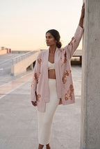 Chaqueta kimono Anzu, flores de lentejuelas, rosa empolvado: modelo con un brazo en alto, en la azotea de un aparcamiento de hormigón claro