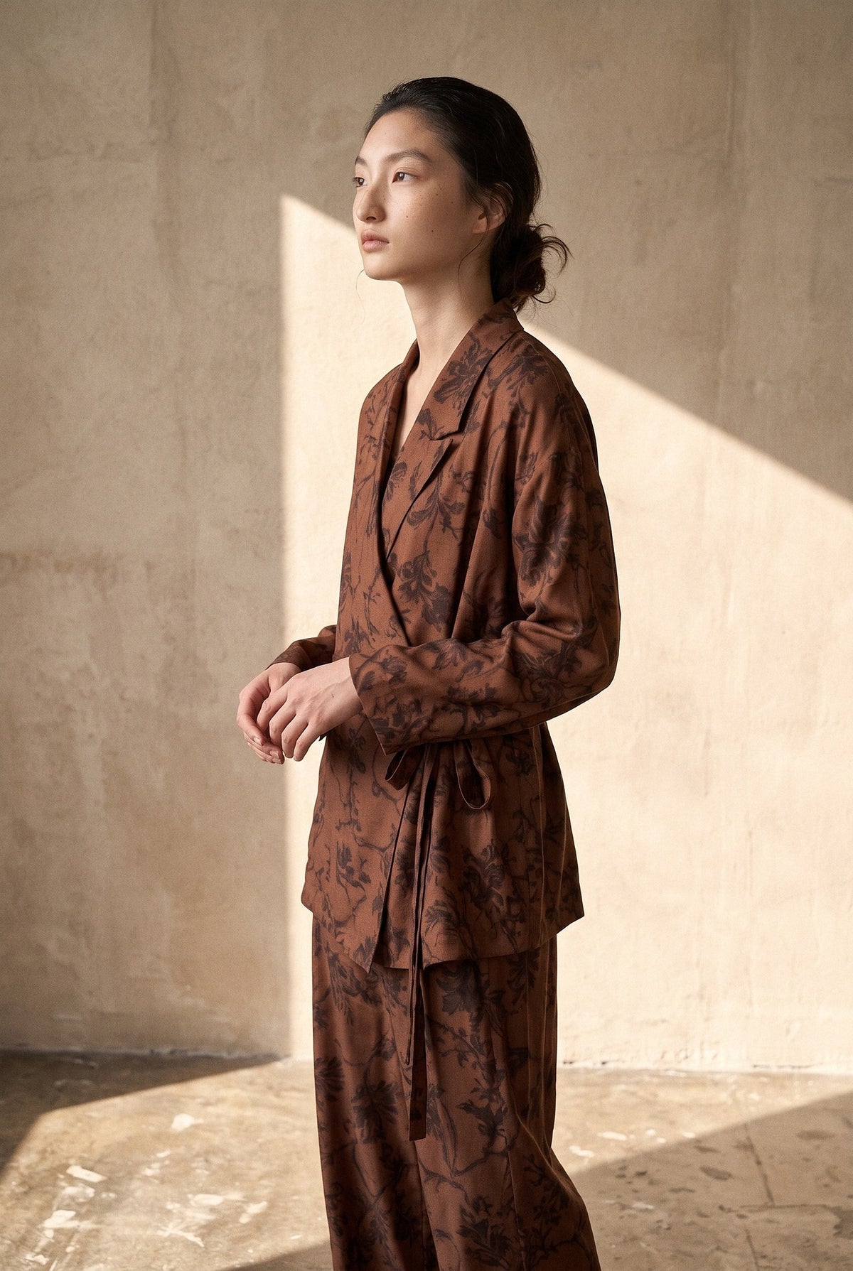 Conjunto kimono Kogecha, chaqueta y pantalón, marrón tostado: modelo con las manos entrelazadas, en estudio, ante una pared de yeso color arena