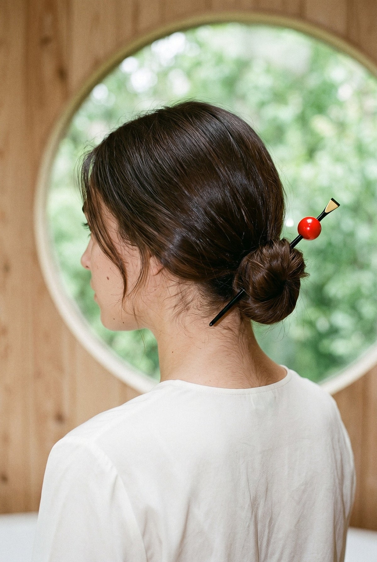 Horquilla kanzashi Tama, esfera de color: vista de tres cuartos de espaldas, con la horquilla en el moño, en una sala de cedro claro con una ventana redonda
