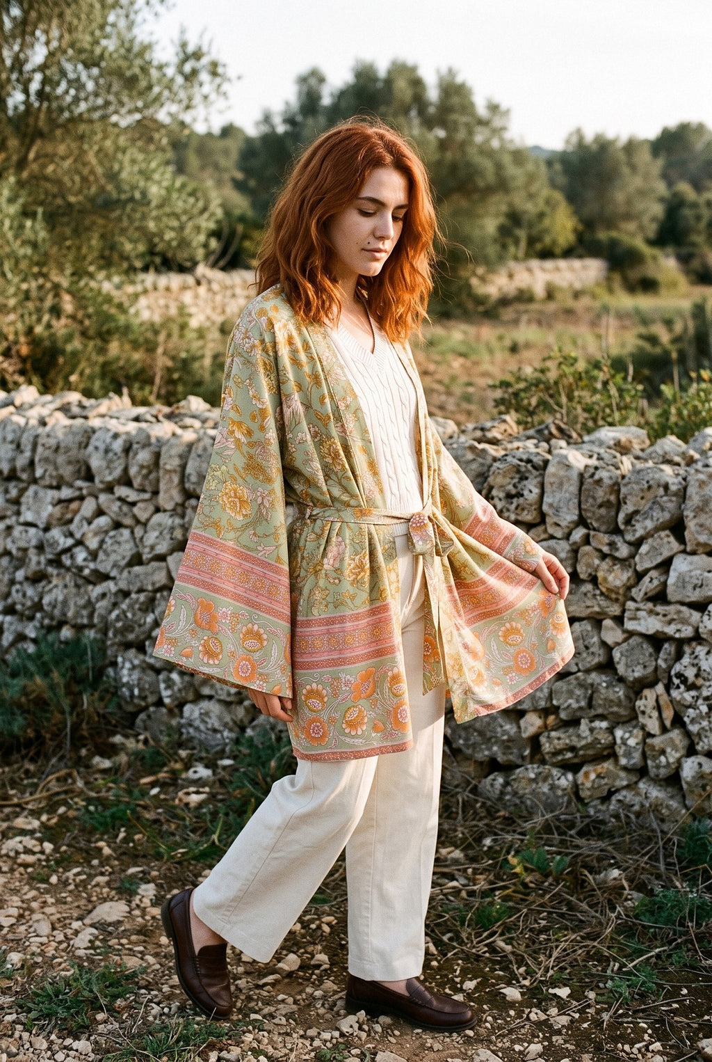 Kimono corto Asahi, flores, verde salvia: modelo caminando, junto a un muro de piedra seca en Mallorca