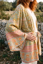 Kimono corto Asahi, flores, verde salvia: detalle de la manga y del estampado, junto a un muro de piedra seca en Mallorca