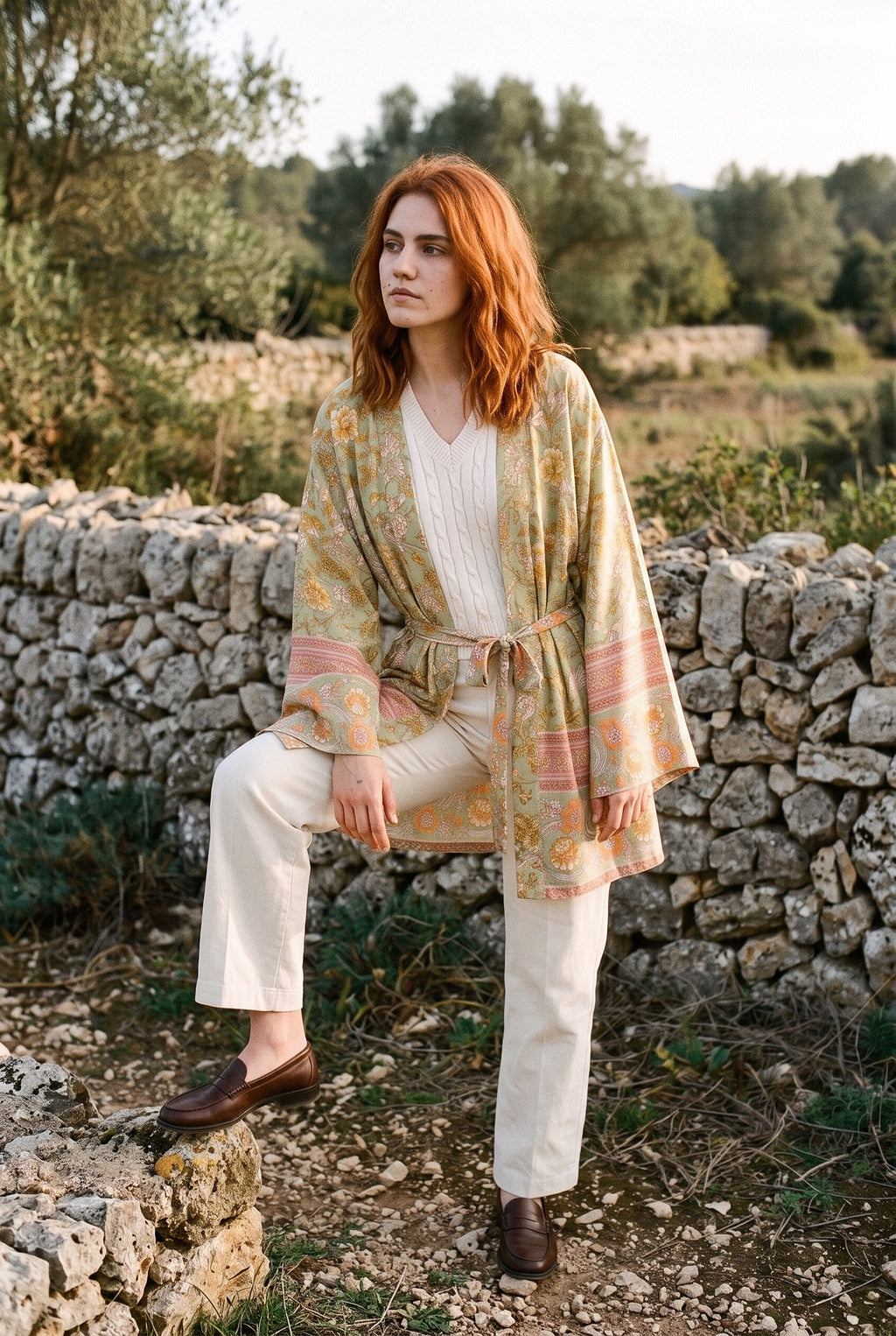 Kimono corto Asahi, flores, verde salvia: modelo con un pie en un escalón, junto a un muro de piedra seca en Mallorca