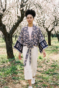 Kimono corto Hai, flores, azul marino y rosa: modelo caminando hacia la cámara, en un almendral en flor de Mallorca
