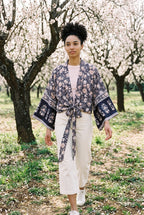 Kimono corto Hai, flores, azul marino y rosa: modelo caminando hacia la cámara, en un almendral en flor de Mallorca