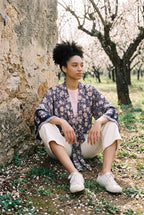 Kimono corto Hai, flores, azul marino y rosa: modelo sentada contra la pared, en un almendral en flor de Mallorca