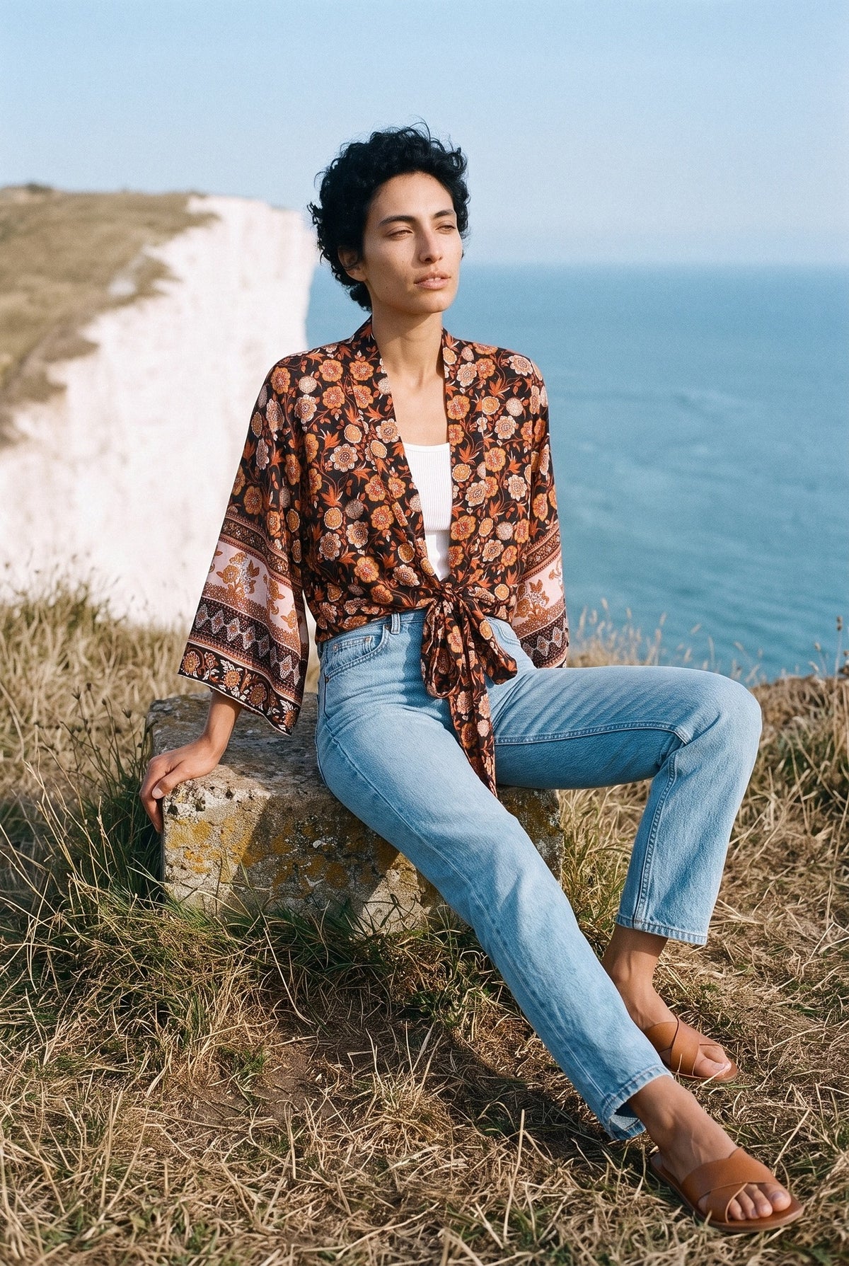 Kimono corto Kaki, flores, negro y teja: modelo sentada con una pierna estirada, en lo alto de acantilados blancos frente al mar