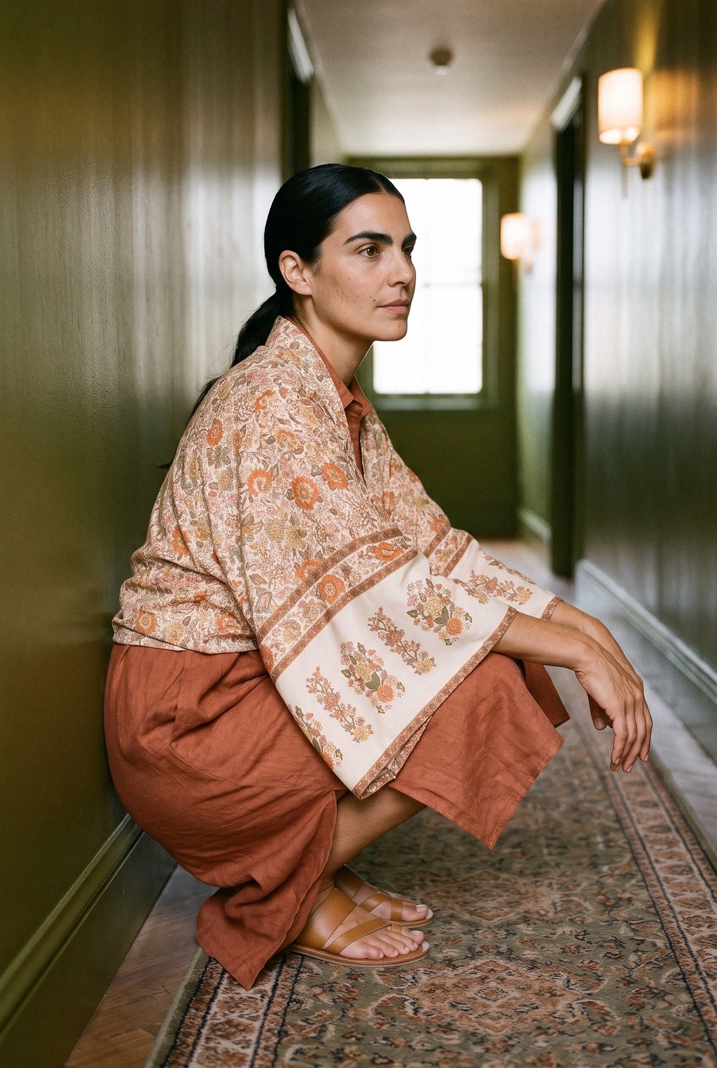 Kimono corto Kitsune, flores, crudo: modelo agachada, en un pasillo de hotel de paredes verde oliva lacadas