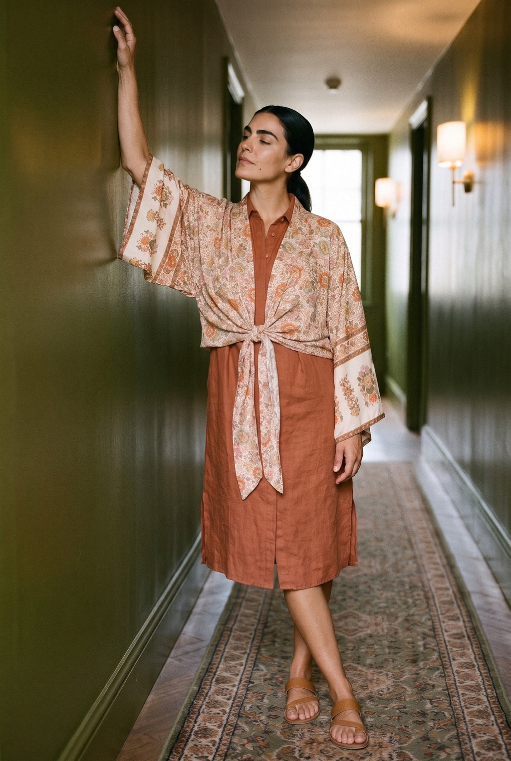 Kimono corto Kitsune, flores, crudo: modelo con un brazo en alto, en un pasillo de hotel de paredes verde oliva lacadas