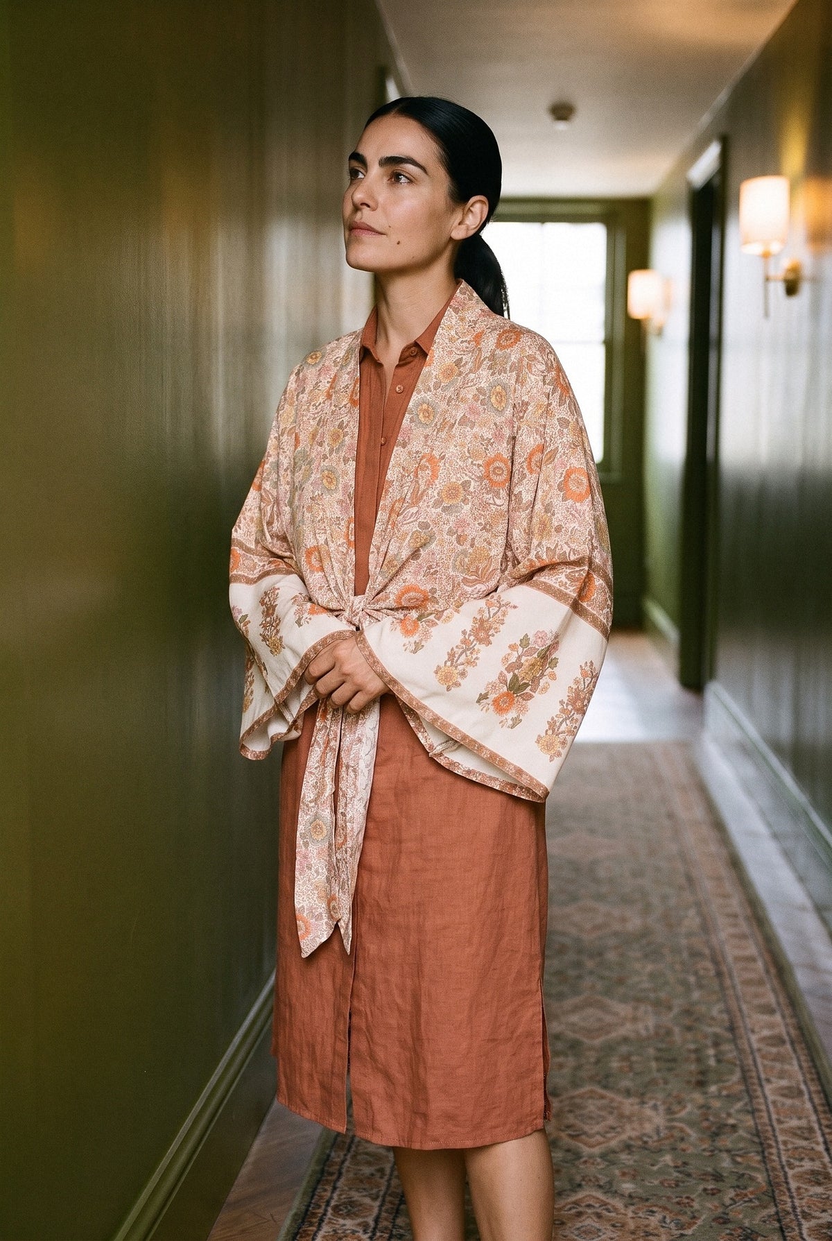 Kimono corto Kitsune, flores, crudo: modelo con las manos dentro de las mangas, en un pasillo de hotel de paredes verde oliva lacadas