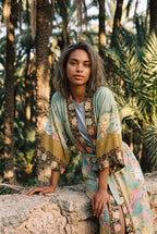 Kimono largo Koke, pavo real y flores, verde salvia: modelo apoyada en un muro, en un palmeral de Elche