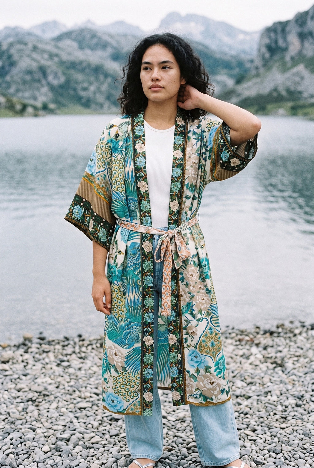 Kimono largo Umi, pavo real y flores, crudo y verde azulado: modelo con una mano en la nuca, a orillas de un lago de los Picos de Europa