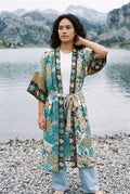 Kimono largo Umi, pavo real y flores, crudo y verde azulado: modelo con una mano en la nuca, a orillas de un lago de los Picos de Europa