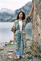 Kimono largo Umi, pavo real y flores, crudo y verde azulado: modelo con un brazo en alto, a orillas de un lago de los Picos de Europa