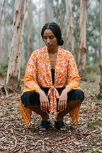 Kimono corto Yamabuki, flores, marfil y naranja: modelo agachada, en un bosque de eucaliptos de Cantabria