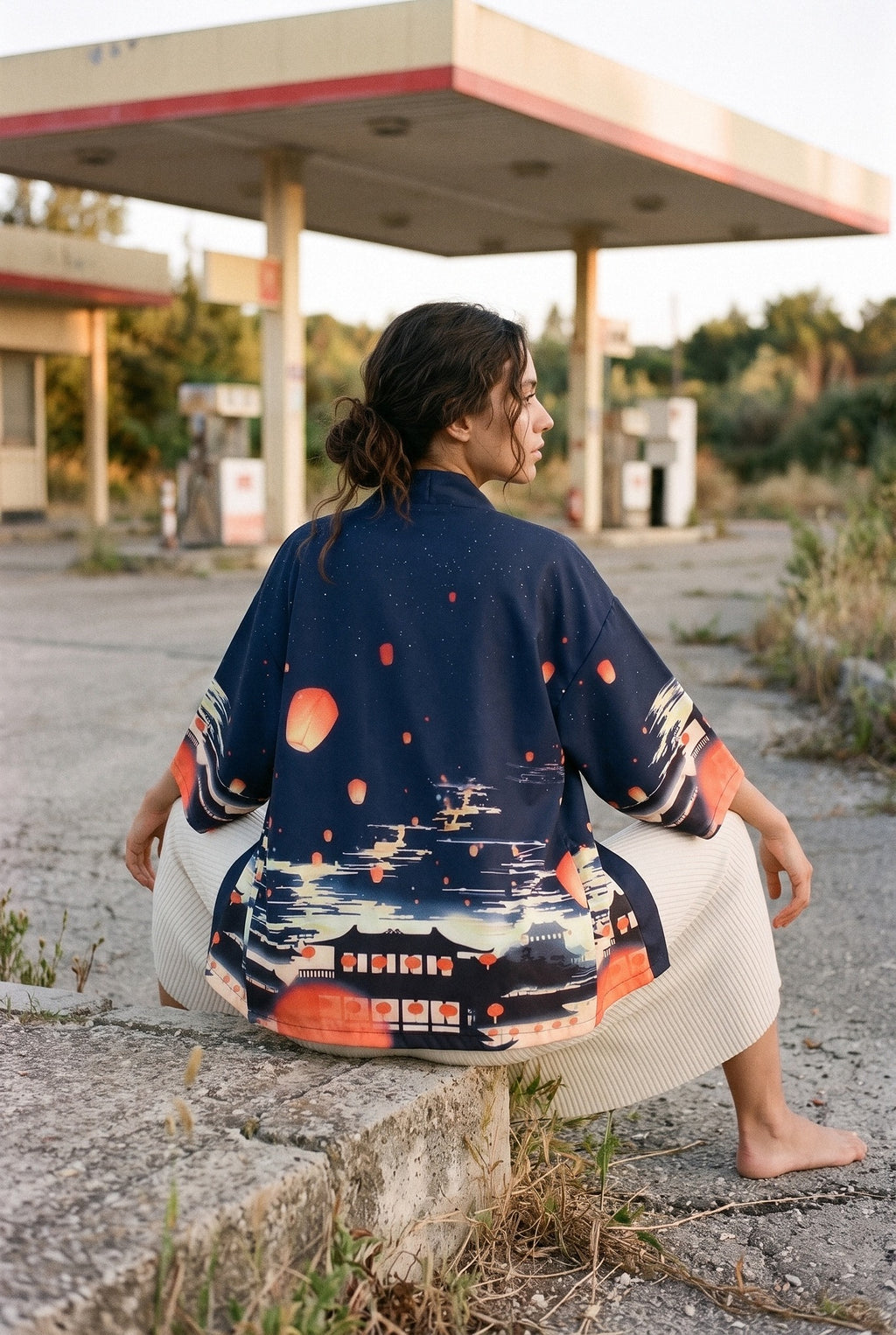 Kimono japonés Chōchin, linternas y ciudad, azul noche: modelo de espaldas, sentada en un bloque, bajo la marquesina de una gasolinera de los años 60