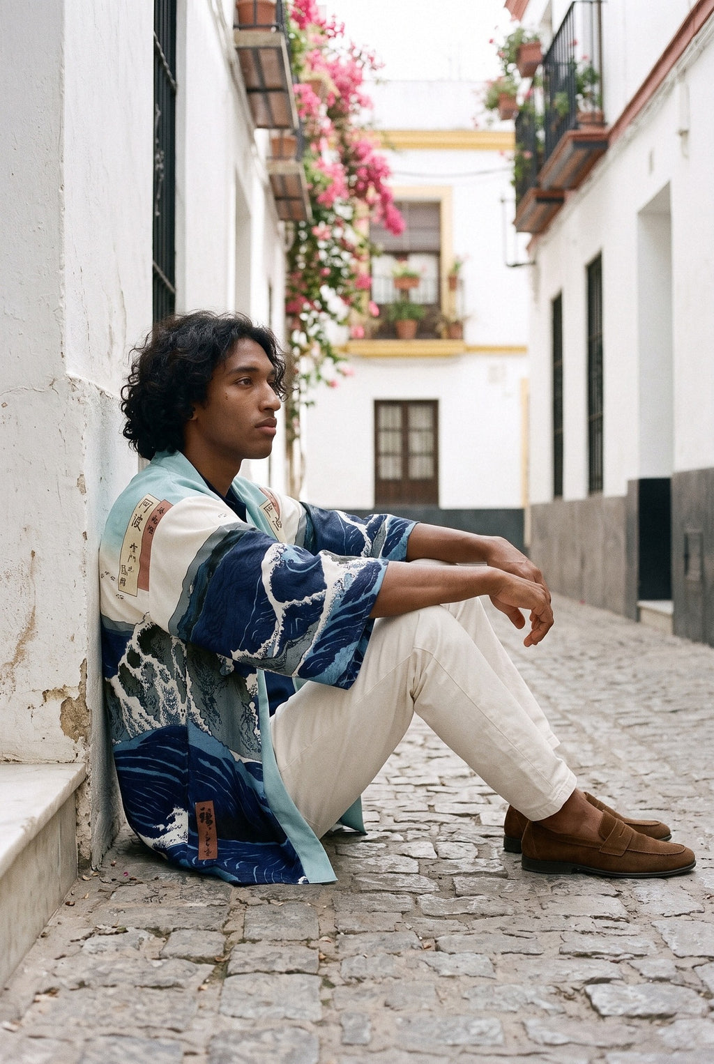 Kimono japonés Kanagawa, olas y remolino, azul: modelo sentado contra la pared, en un callejón de Sevilla con buganvillas