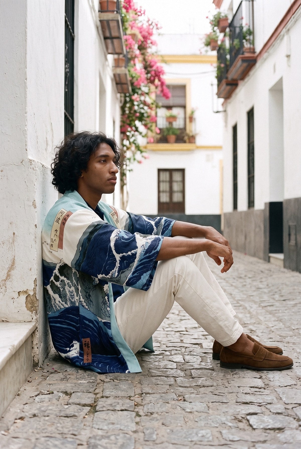 Kimono japonés Kanagawa, olas y remolino, azul: modelo sentado contra la pared, en un callejón de Sevilla con buganvillas
