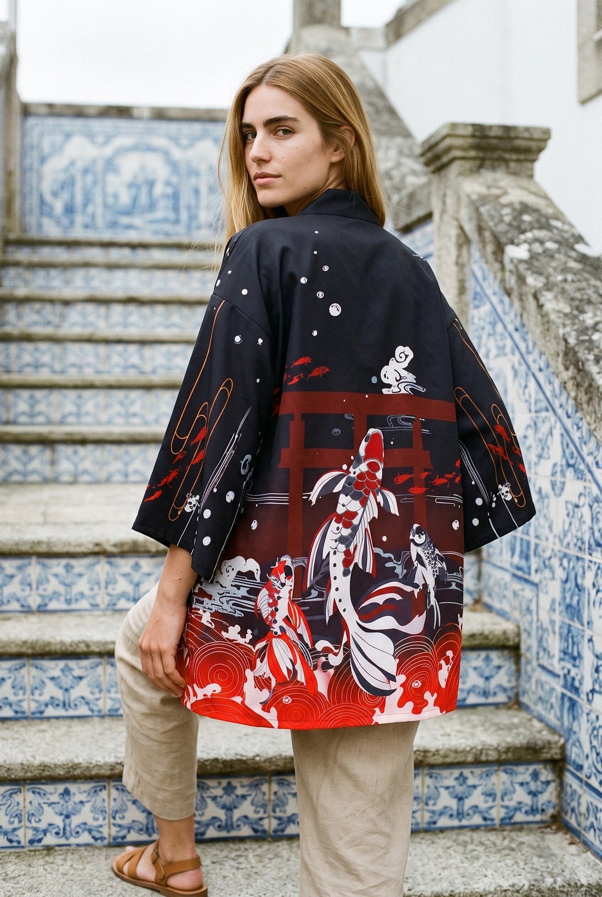 Kimono japonés Mizu, carpas koi y torii, negro y rojo: modelo de espaldas, mirando por encima del hombro, en una escalera de azulejos azules en Galicia