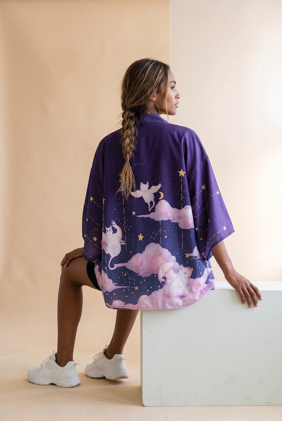 Kimono japonés Yozora, gatos y nubes, violeta noche: modelo de espaldas, sentada en un bloque, en estudio, fondo beige arena con cristal esmerilado