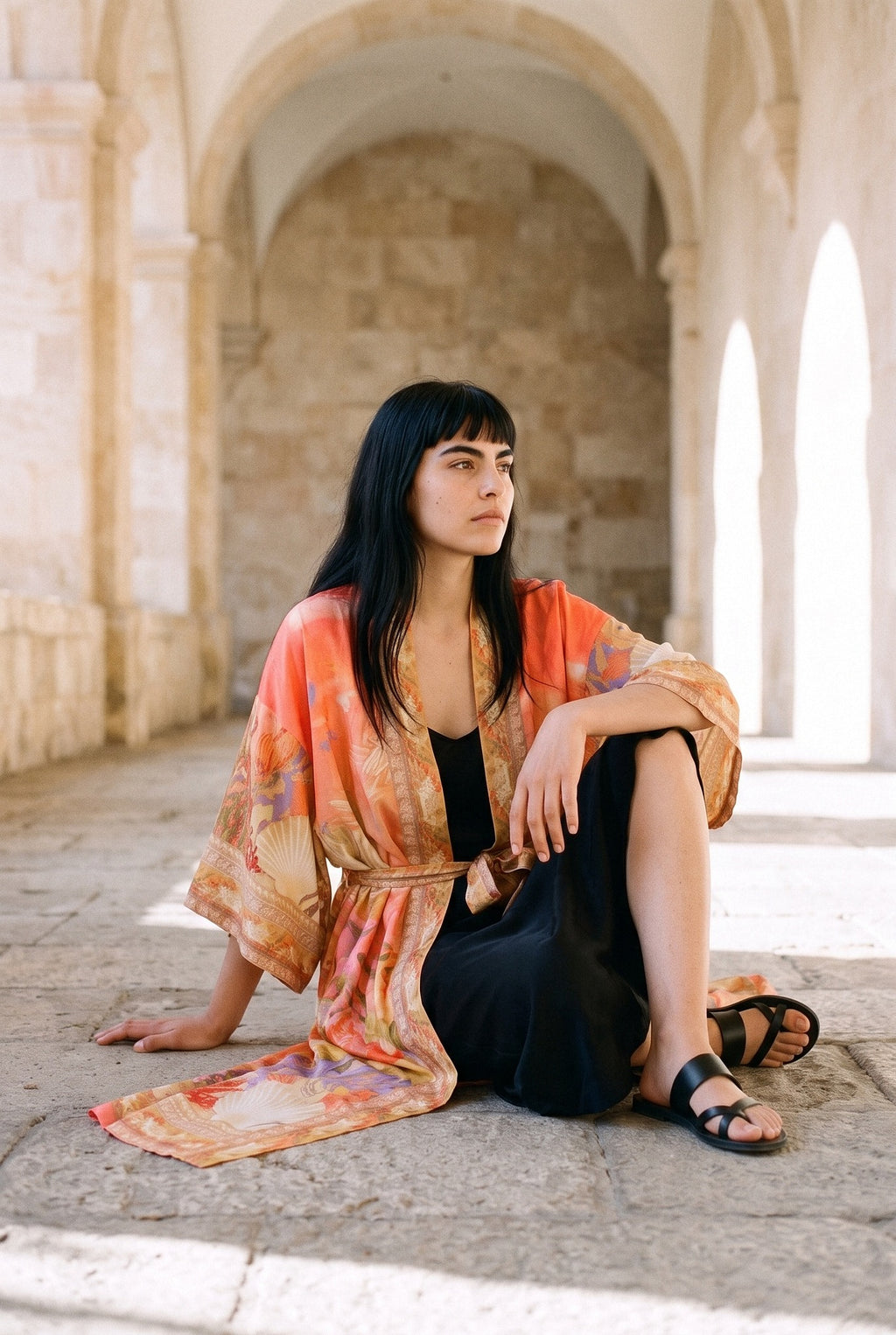 Kimono largo Sangoshō, flores, coral: modelo sentada en el suelo, en un claustro de arcos de arenisca