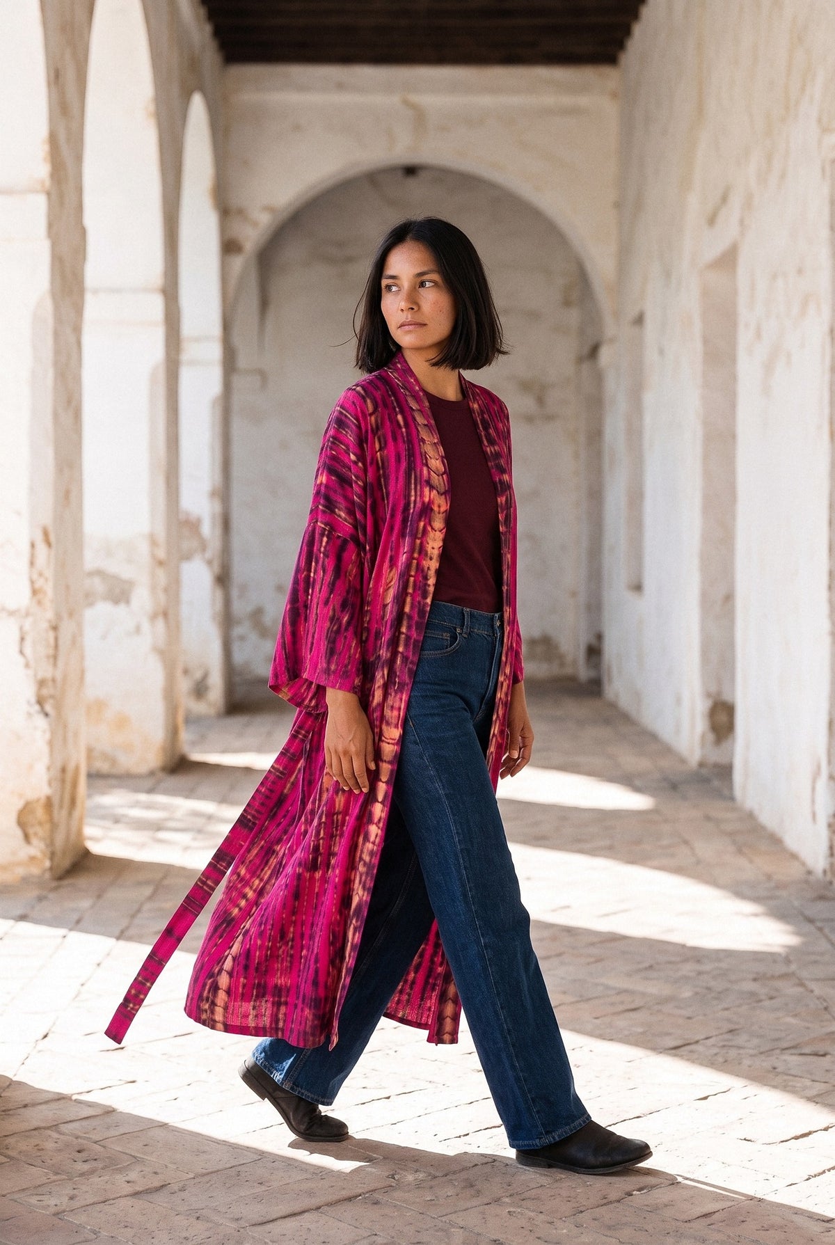 Kimono largo Shibori, efecto tie-dye, magenta: modelo caminando, vista de tres cuartos, en un pasillo de arcos encalados de un convento andaluz