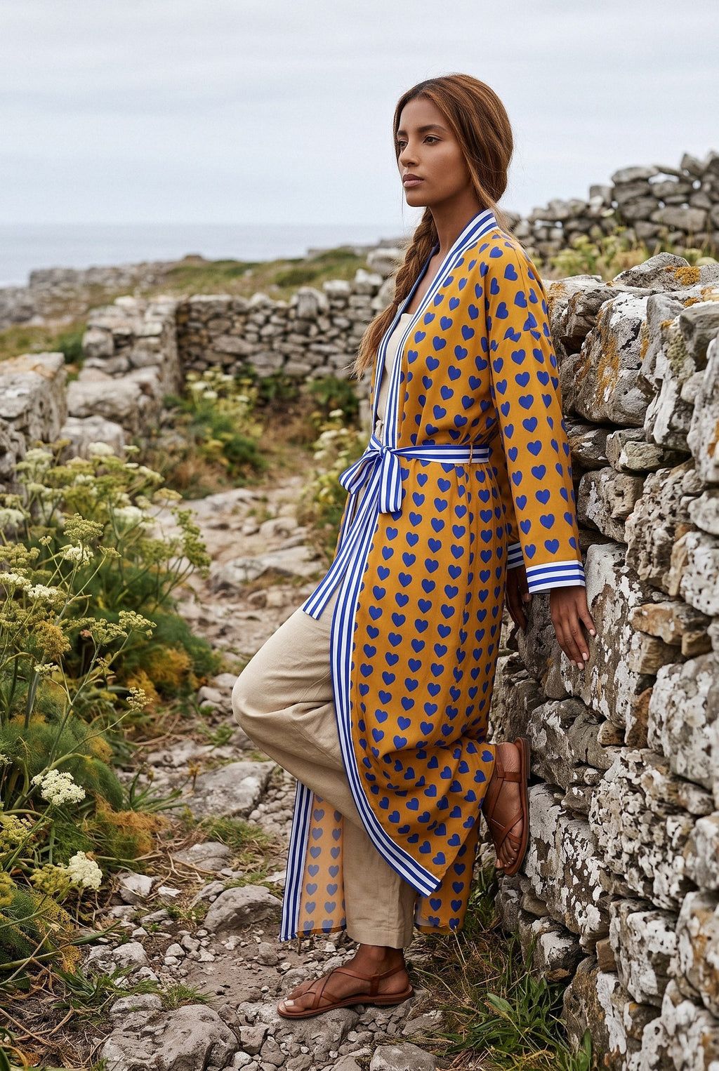 Kimono largo Shimauma, corazones azules, amarillo: modelo apoyada en la pared, en un sendero costero de Galicia